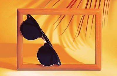 Stylish sunglasses near photo frame on orange background