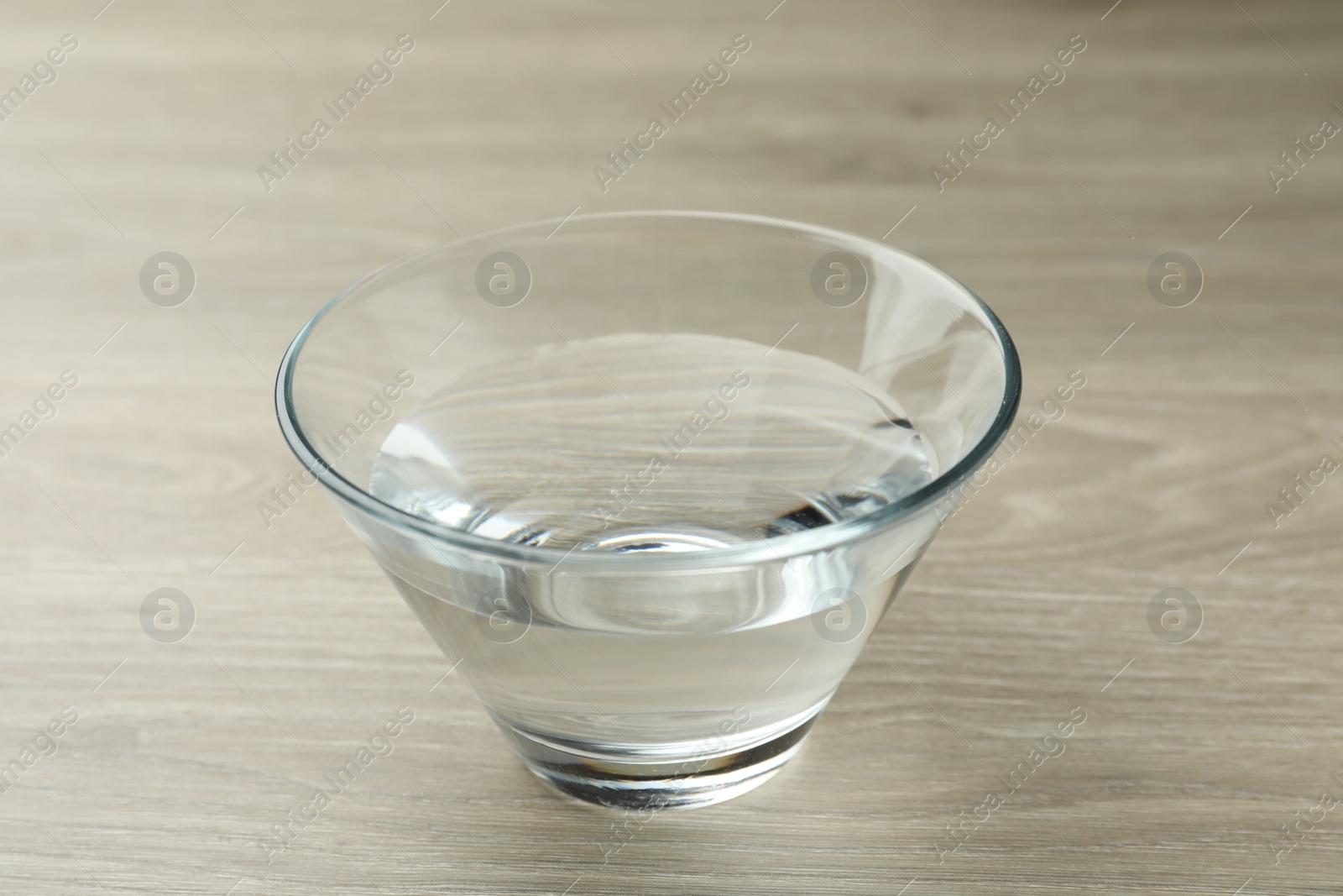 Photo of Glass bowl with water on wooden table, closeup