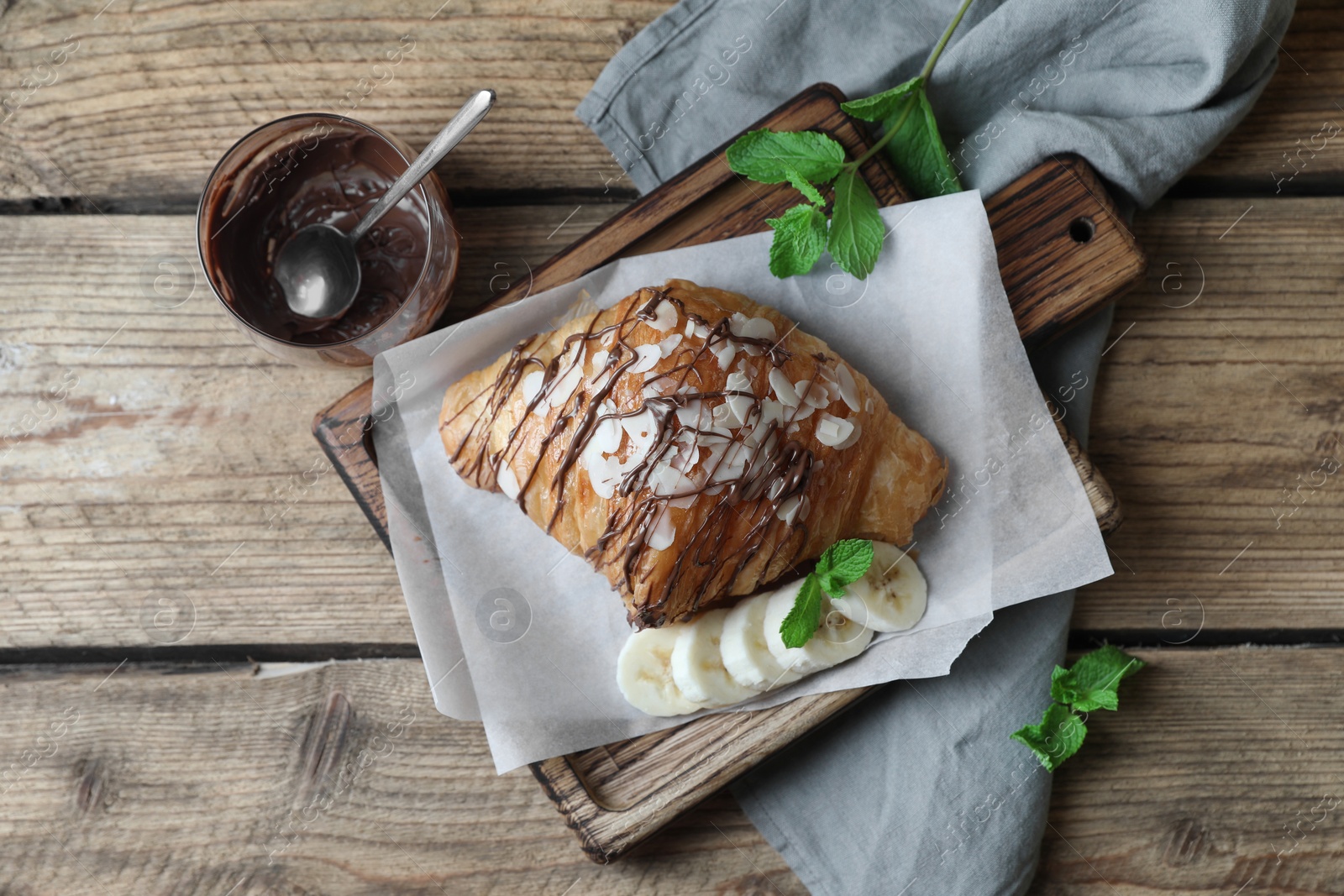 Photo of Delicious croissant with chocolate and banana on wooden table, flat lay