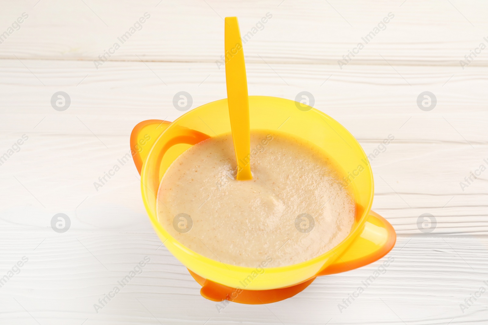 Photo of Baby food. Puree and spoon in bowl on white wooden table