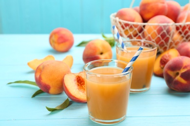 Photo of Natural peach juice and fresh fruits on light blue wooden table
