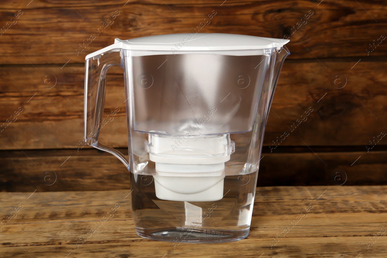 Photo of Filter jug with purified water on wooden table