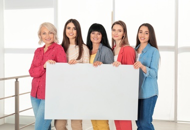 Photo of Group of ladies with empty poster near window indoors, space for text. Women power concept