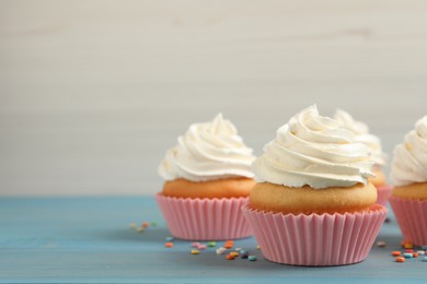 Photo of Delicious cupcakes decorated with cream on light blue wooden table, space for text