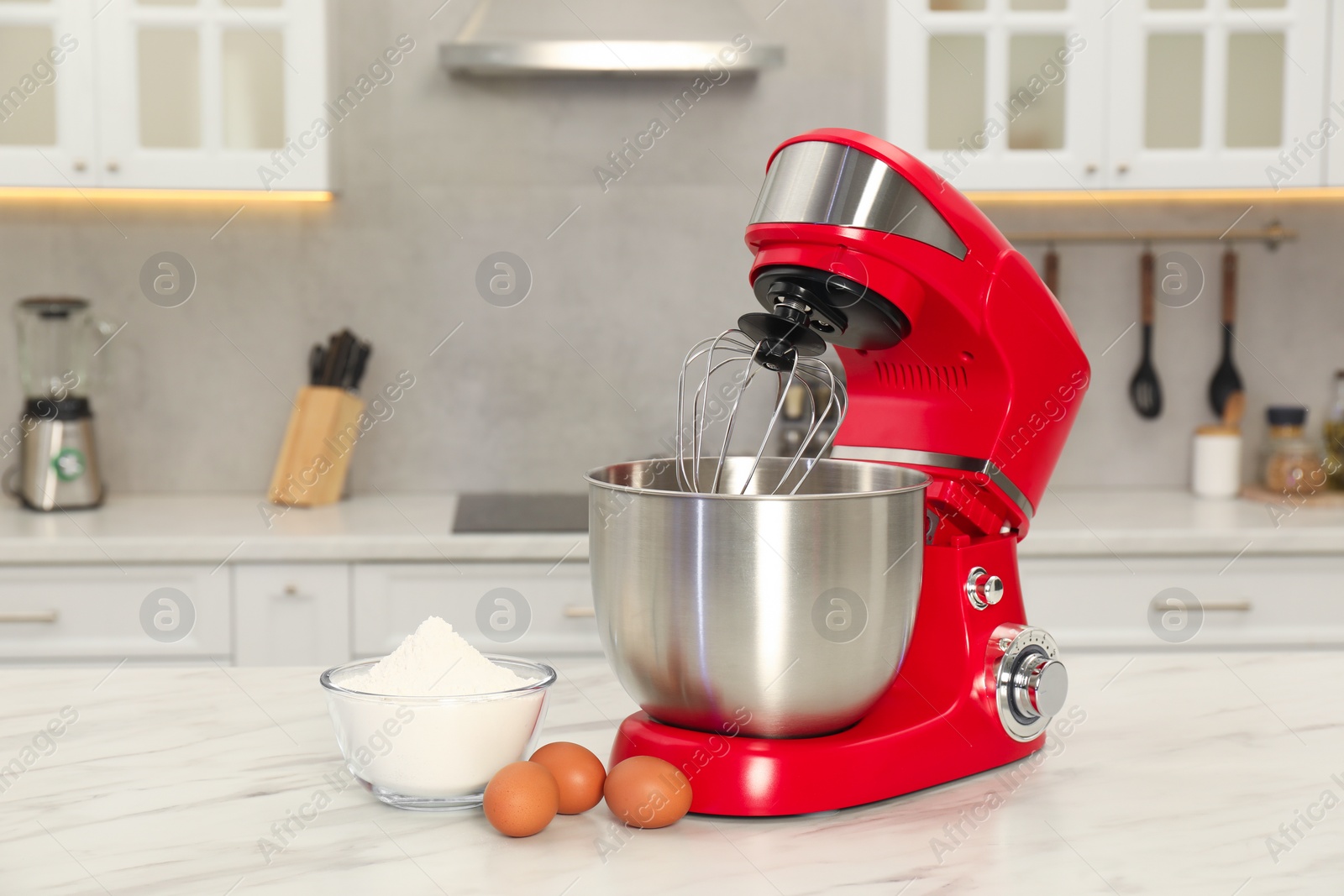 Photo of Modern red stand mixer, eggs and bowl with flour on white marble table in kitchen