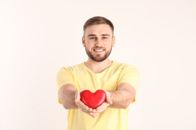 Young man holding wooden heart on white background