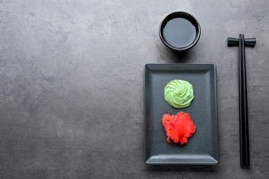 Photo of Swirl of wasabi paste, pickled ginger, soy sauce and chopsticks on grey table, flat lay. Space for text