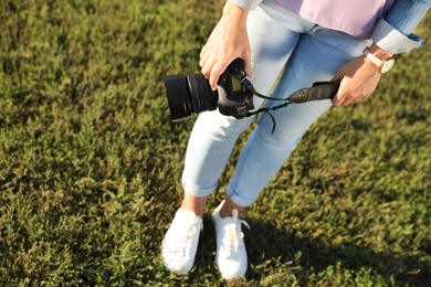 Photo of Young female photographer holding professional camera outdoors. Space for text