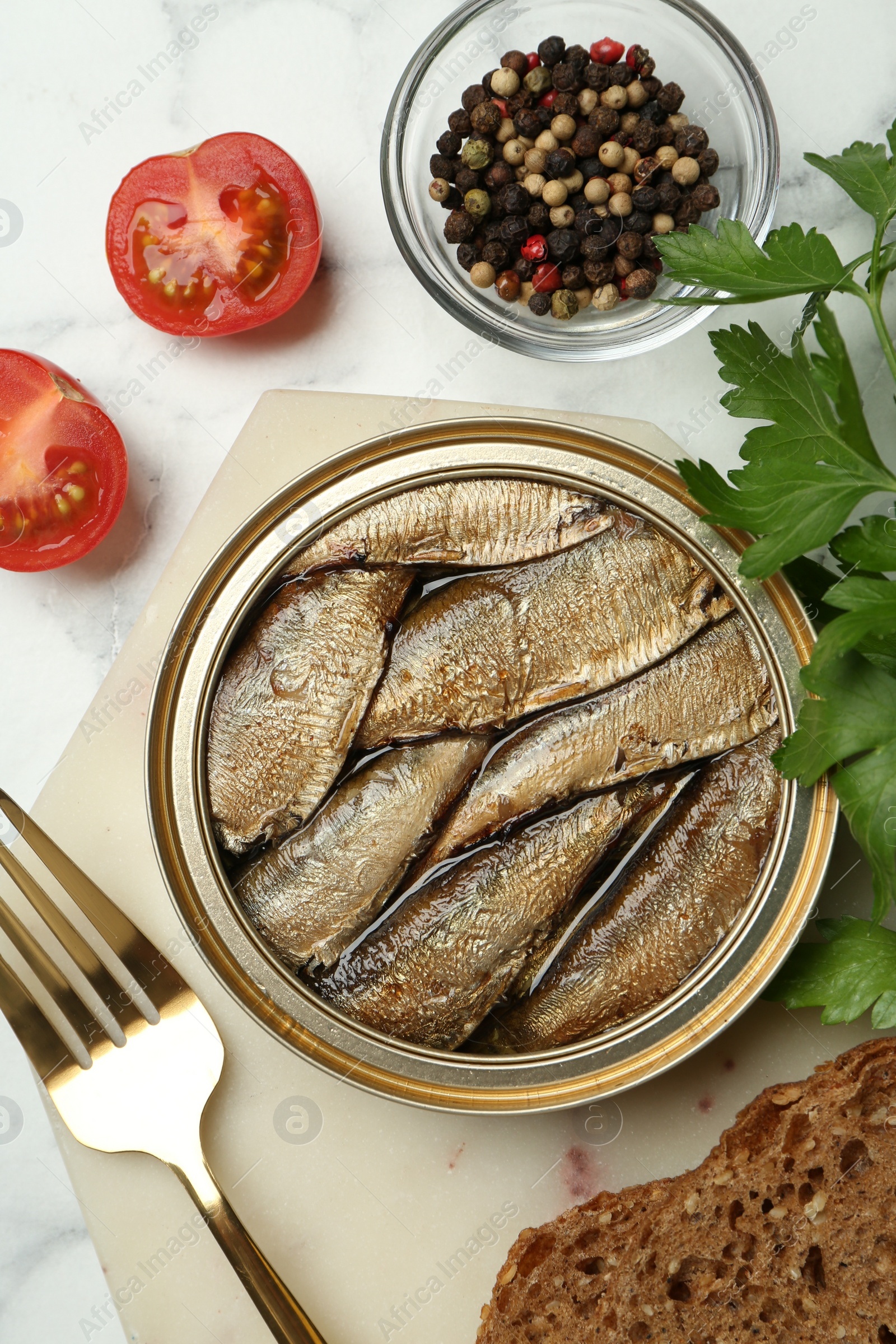 Photo of Tin can with tasty sprats served on white marble table, flat lay