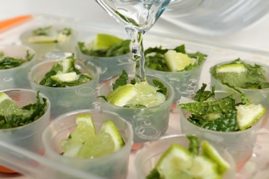 Pouring water into ice cube tray with lime slices and mint, closeup