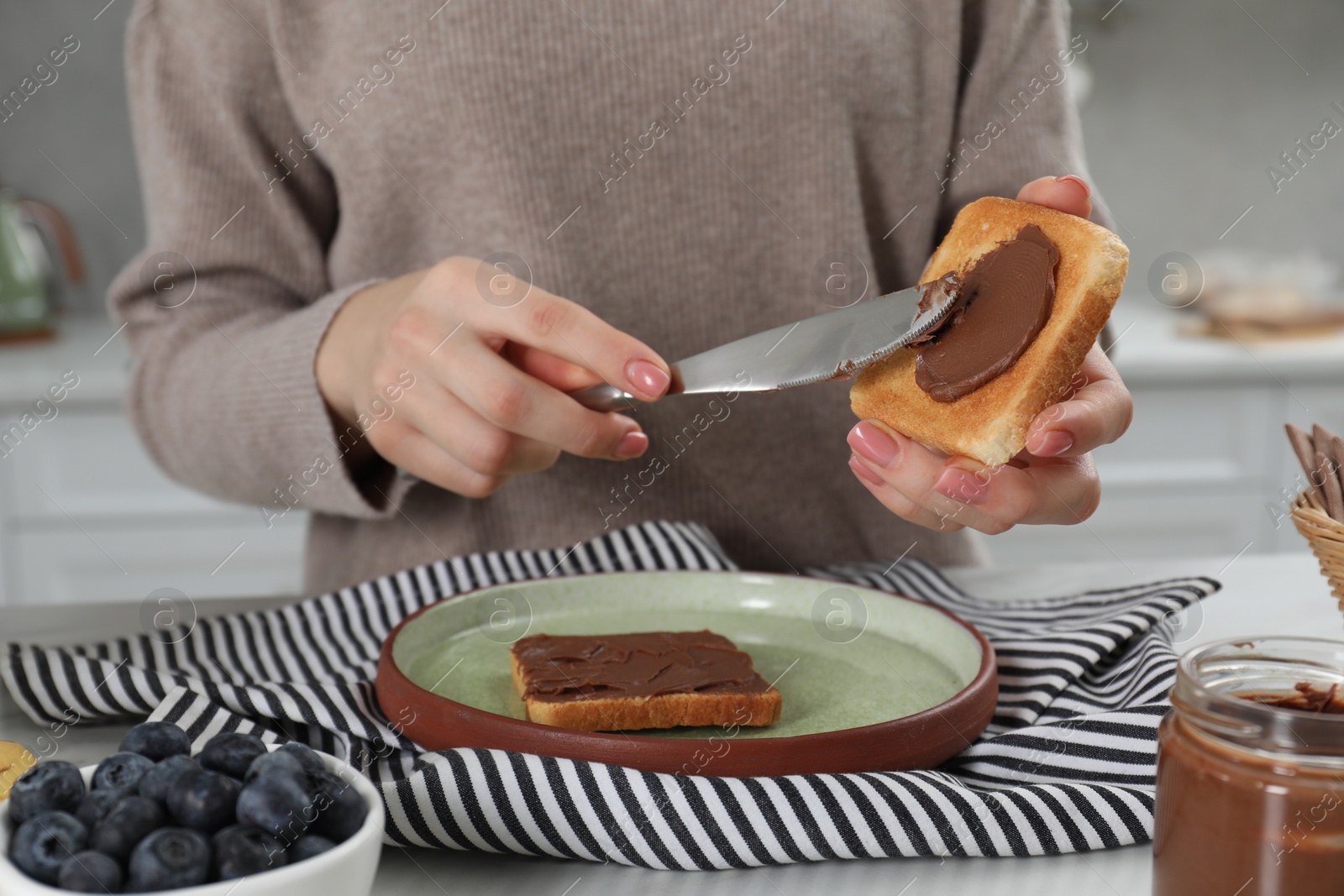 Photo of Woman spreading tasty nut butter onto toast at table, closeup