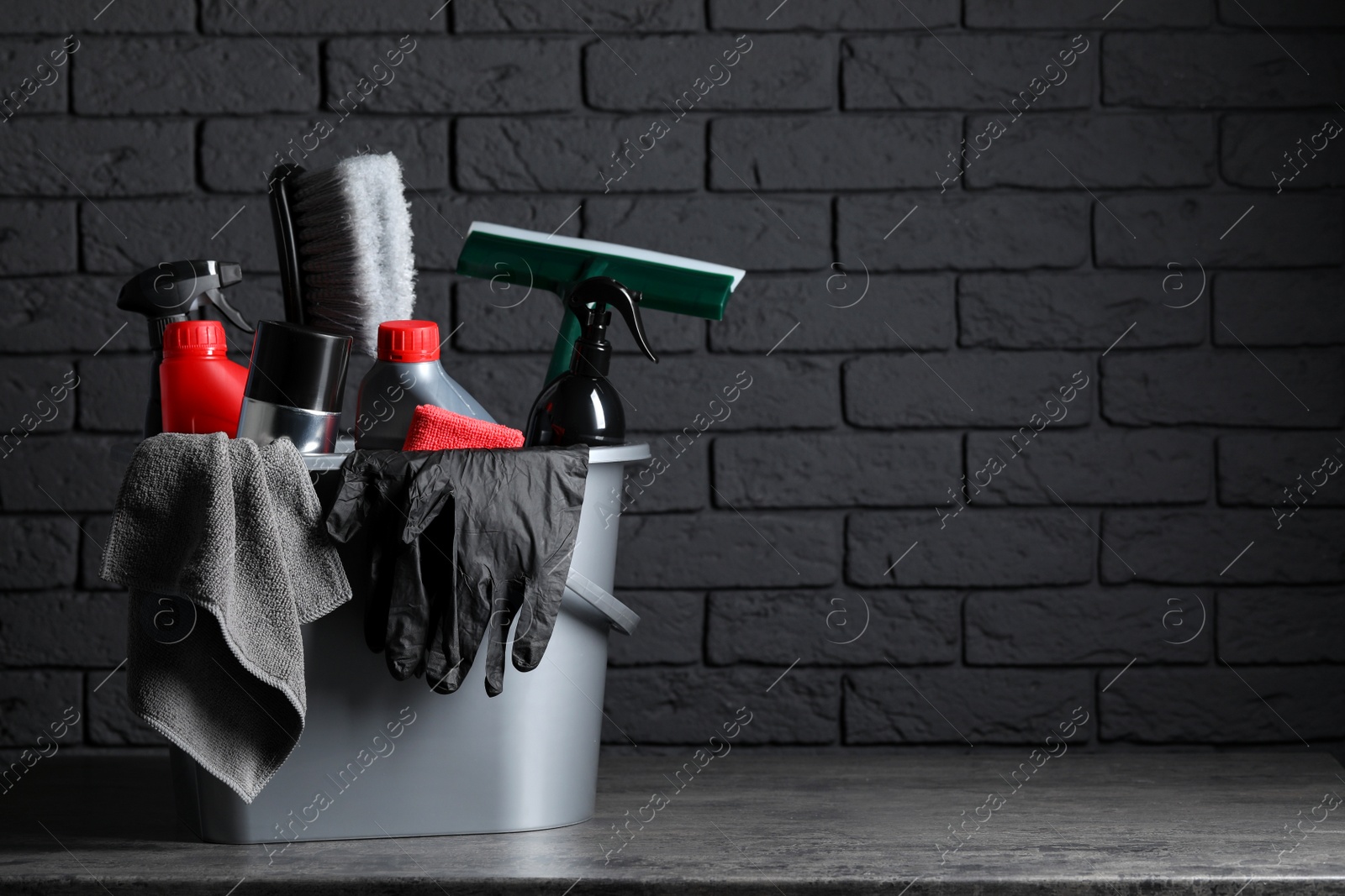 Photo of Different car cleaning products in bucket on table near black brick wall, space for text