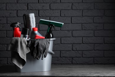 Different car cleaning products in bucket on table near black brick wall, space for text