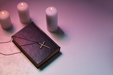 Photo of Cross, burning candles and Bible on textured table in color lights, above view with space for text. Religion of Christianity