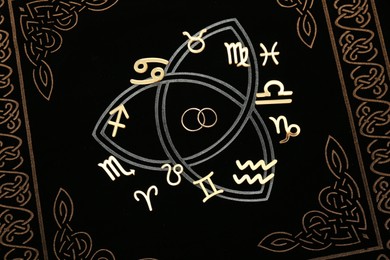 Photo of Zodiac signs and wedding rings on book, flat lay