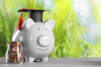 Scholarship concept. Glass jar with coins, piggy bank and graduation cap on grey table, space for text