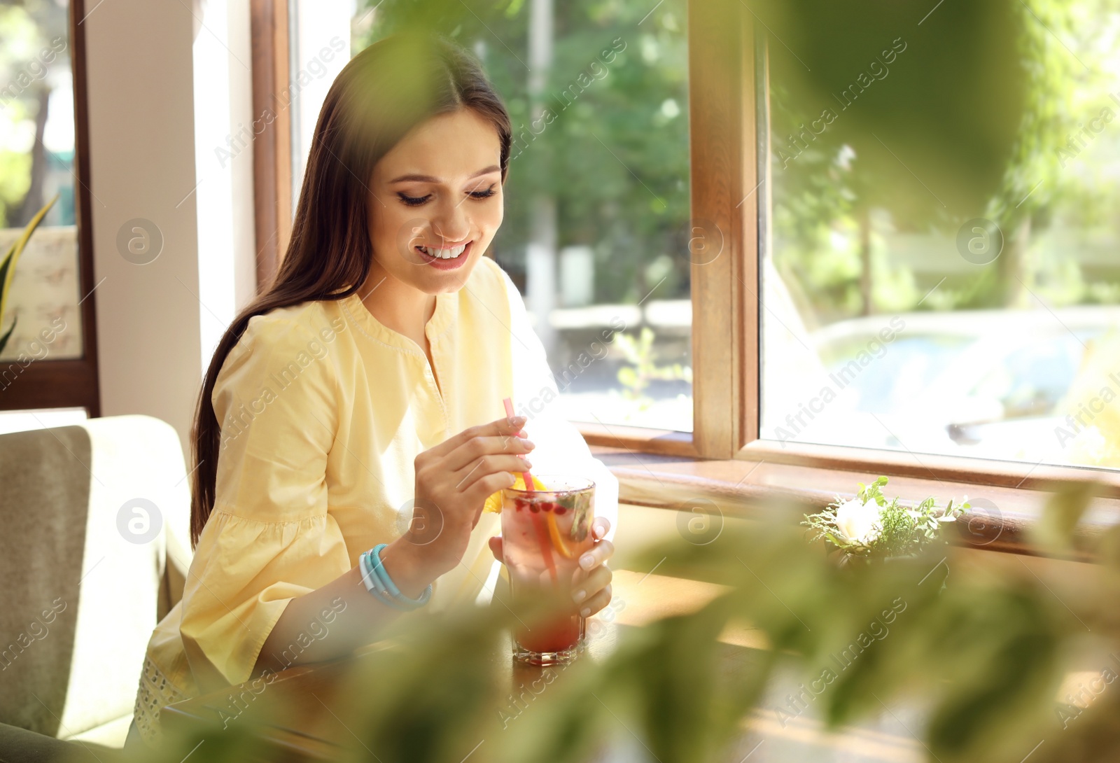 Photo of Young woman with glass of tasty natural lemonade in cafe. Detox drink