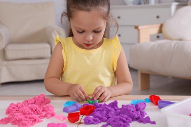 Cute little girl playing with bright kinetic sand at table in room
