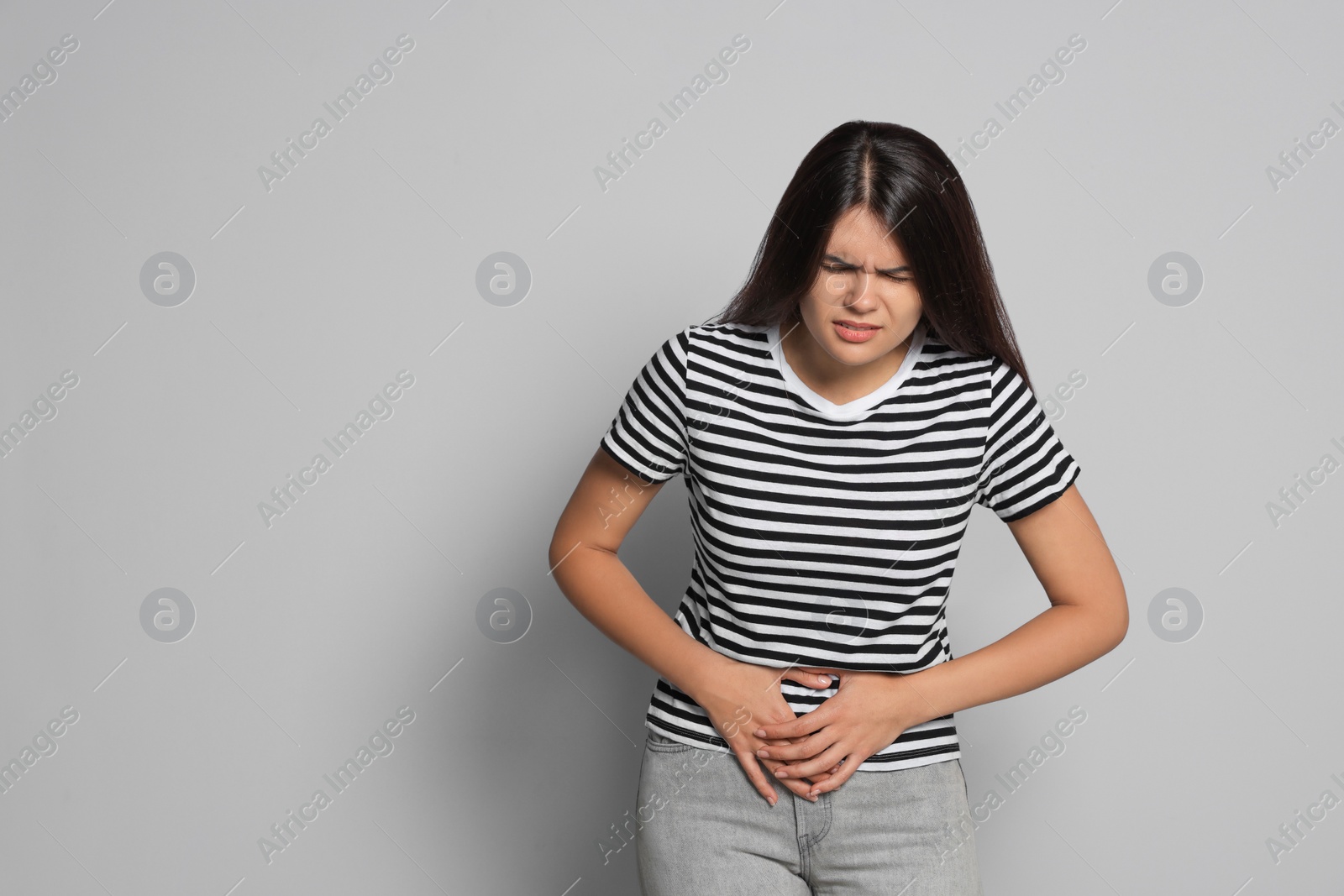 Photo of Young woman suffering from menstrual pain on grey background, space for text