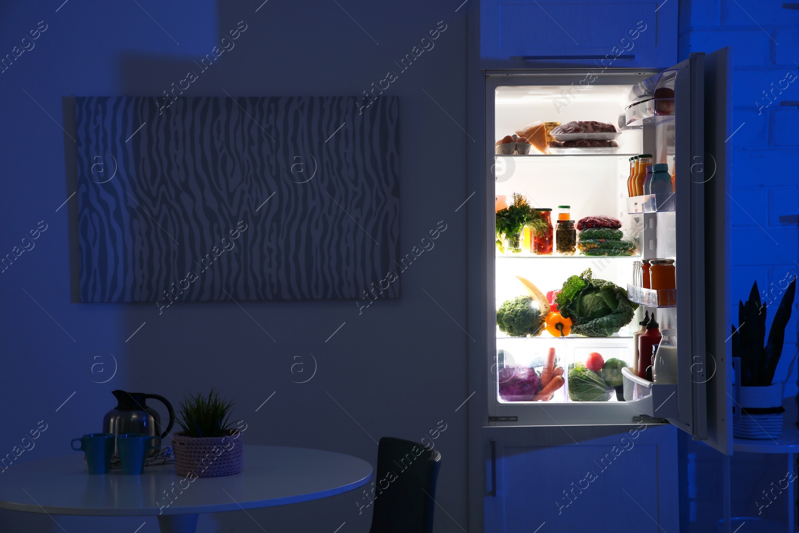 Photo of Stylish kitchen interior with refrigerator full of products at night