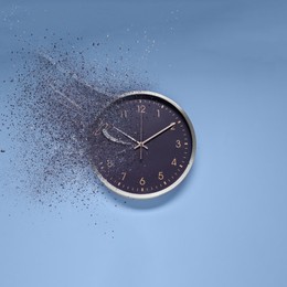 Flow of time. Analog clock dissolving on light blue background