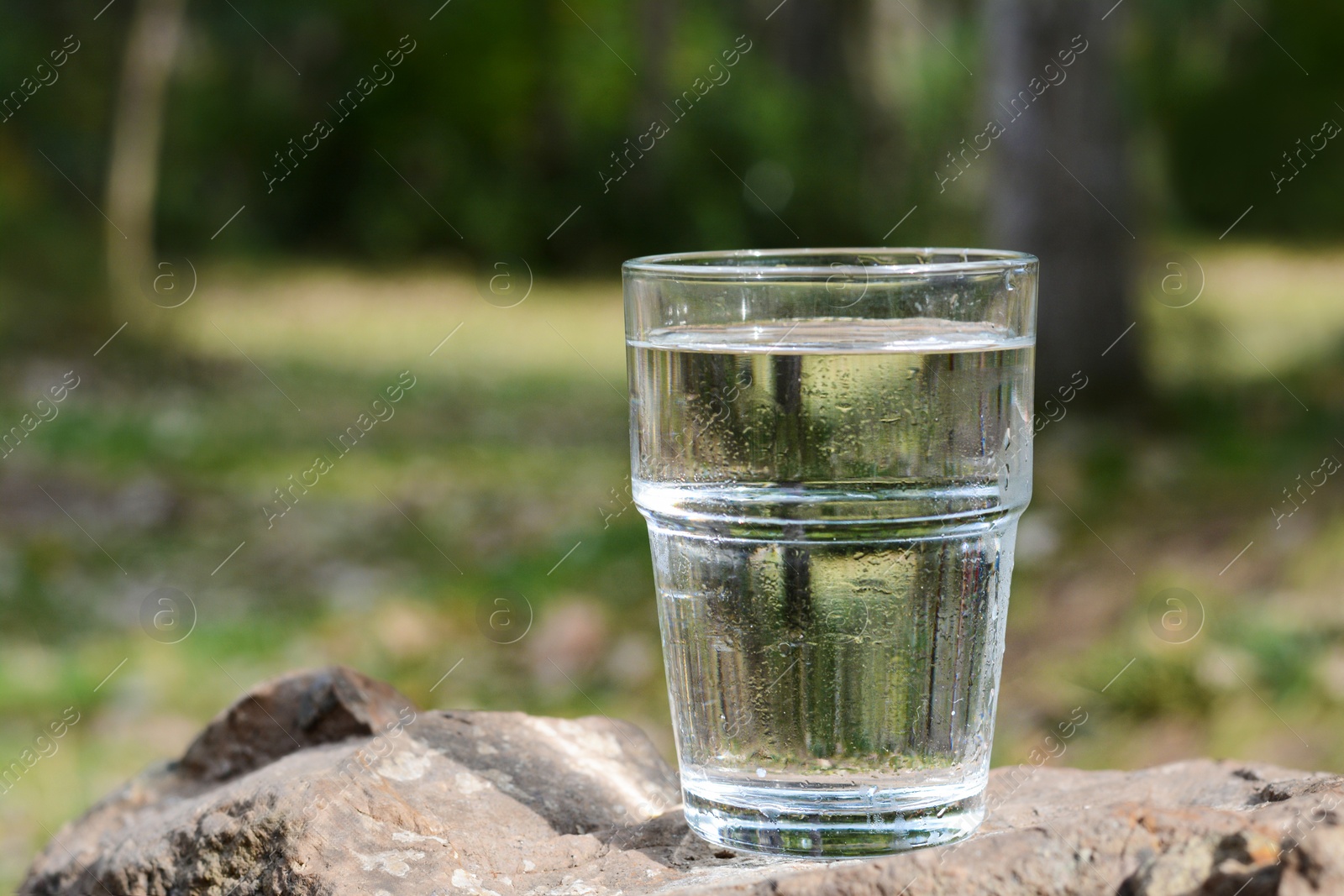 Photo of Glass of water on stone outdoors, space for text