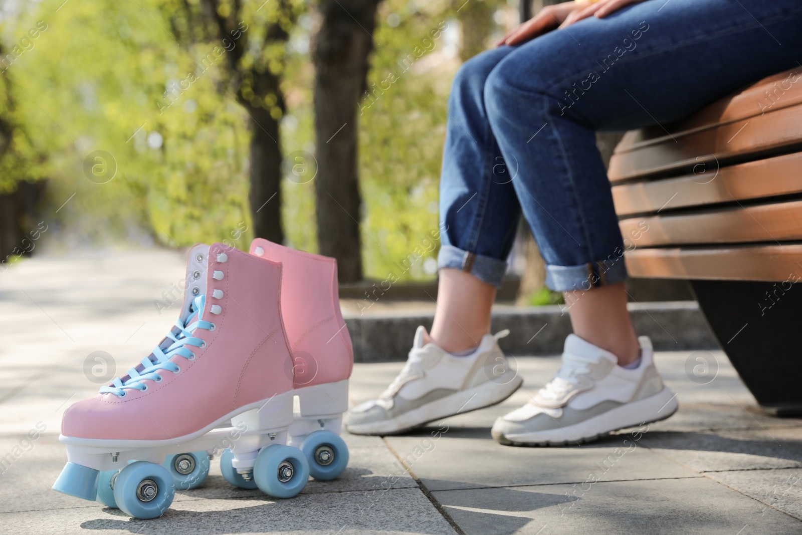 Photo of Woman with stylish pink roller skates sitting on bench outdoors, closeup