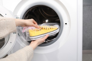 Photo of Woman putting stylish sneakers into washing machine, closeup