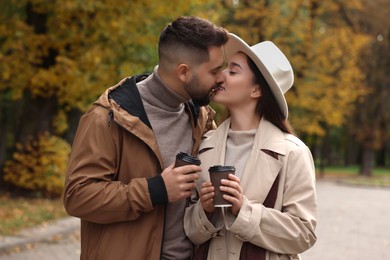 Photo of Happy young couple with cups of coffee spending time together in autumn park