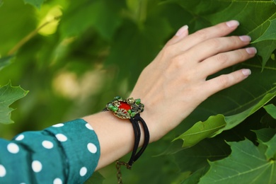 Photo of Young woman wearing beautiful metal bracelet with carnelian and gemstones outdoors, closeup