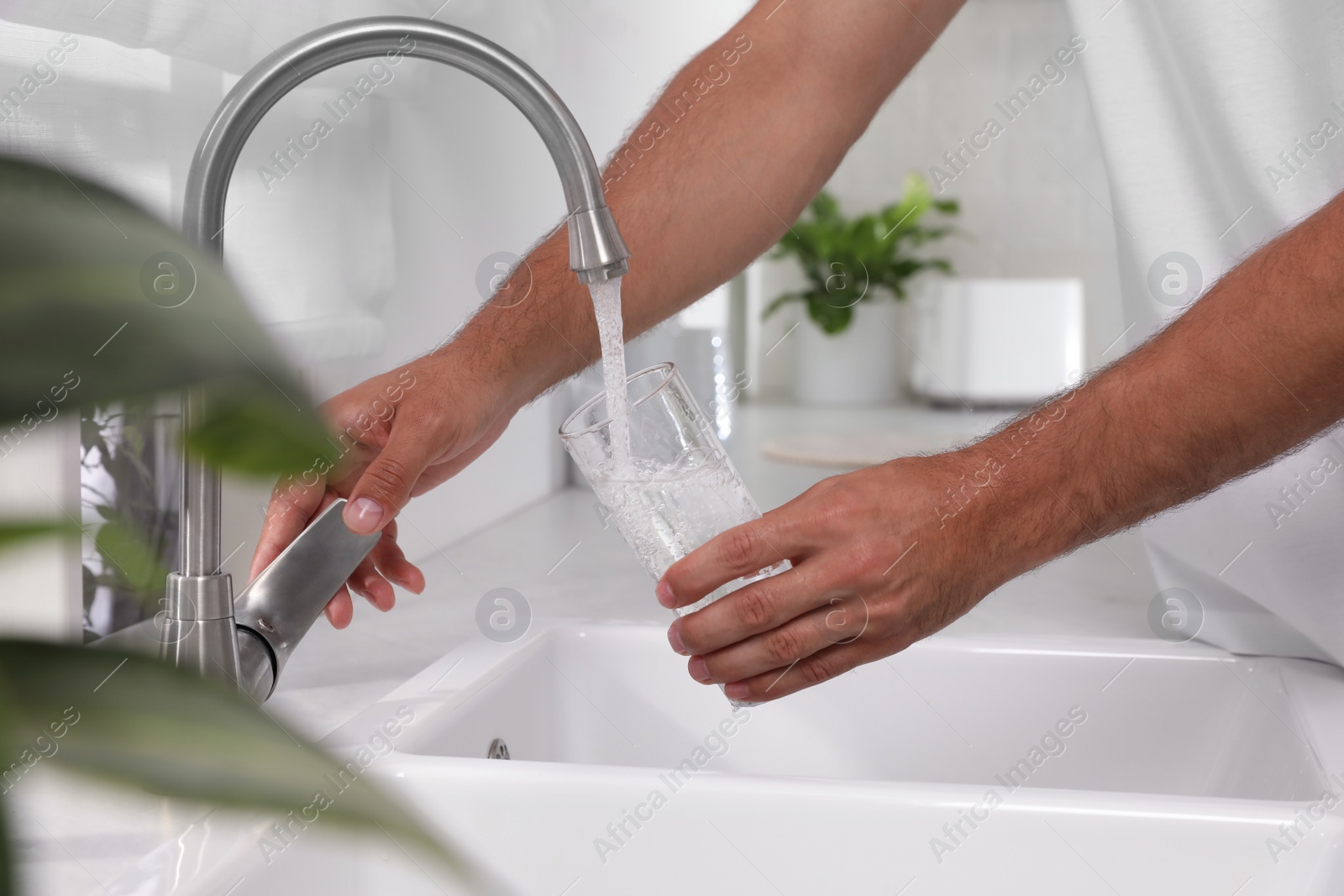 Photo of Man filling glass with water from tap at home, closeup