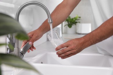 Man filling glass with water from tap at home, closeup