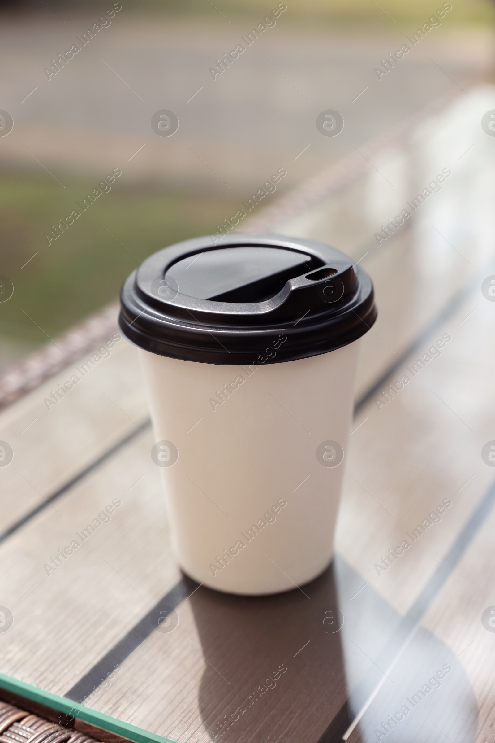 Photo of Paper takeaway cup on glass table outdoors. Coffee to go