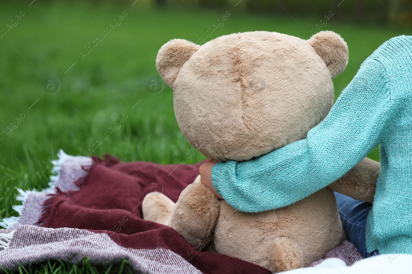 Photo of Little girl with teddy bear on plaid outdoors, closeup. Space for text