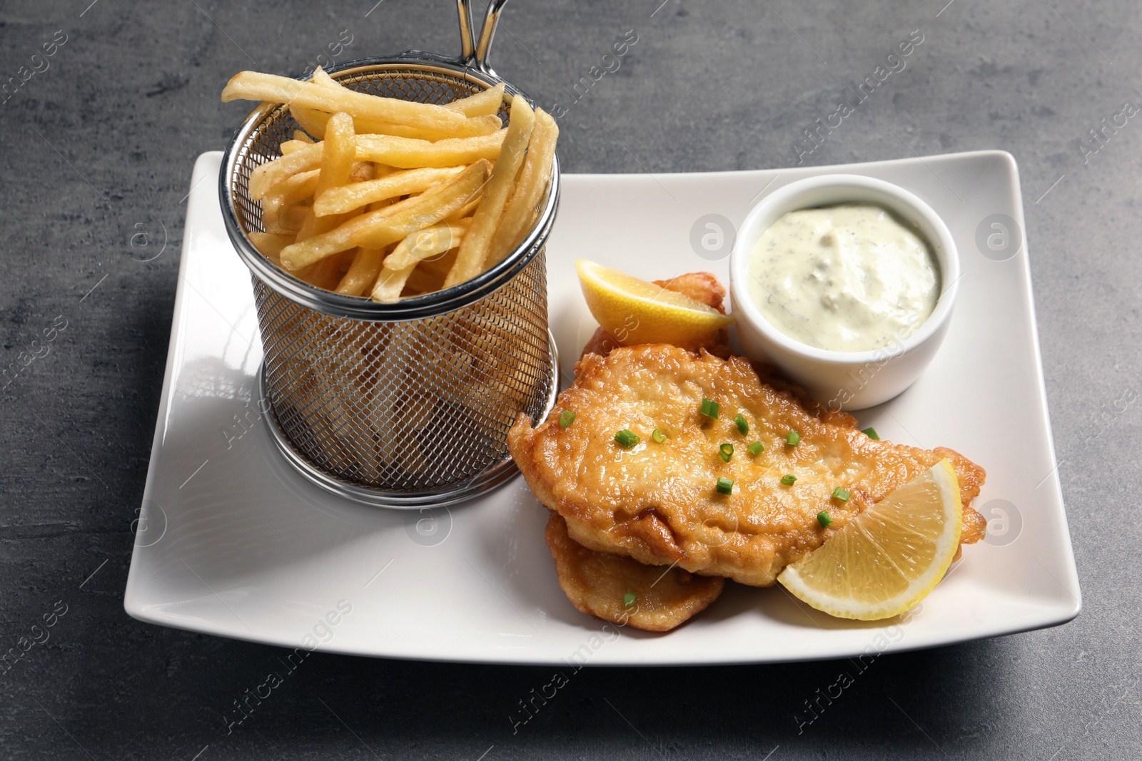 Photo of Plate with British traditional fish and potato chips on grey table