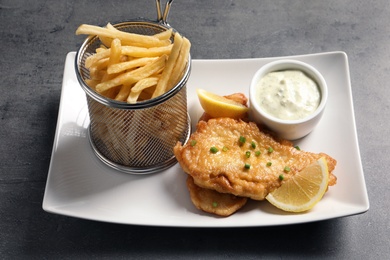 Photo of Plate with British traditional fish and potato chips on grey table