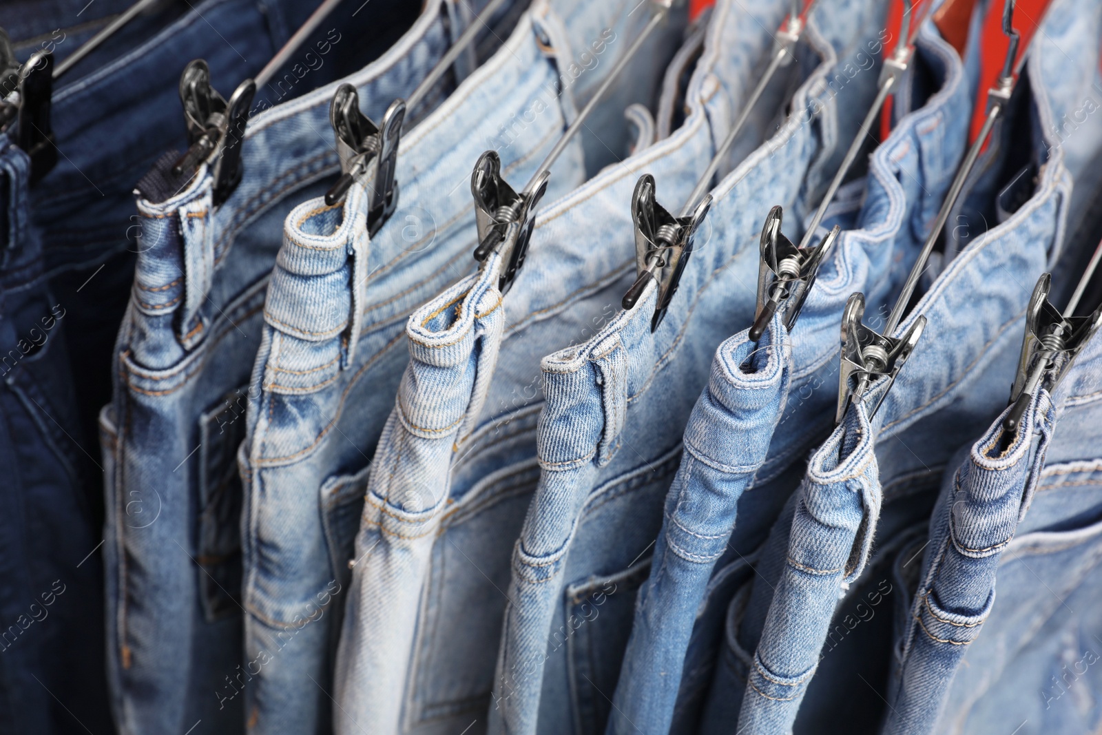 Photo of Metal hangers with different stylish jeans, closeup