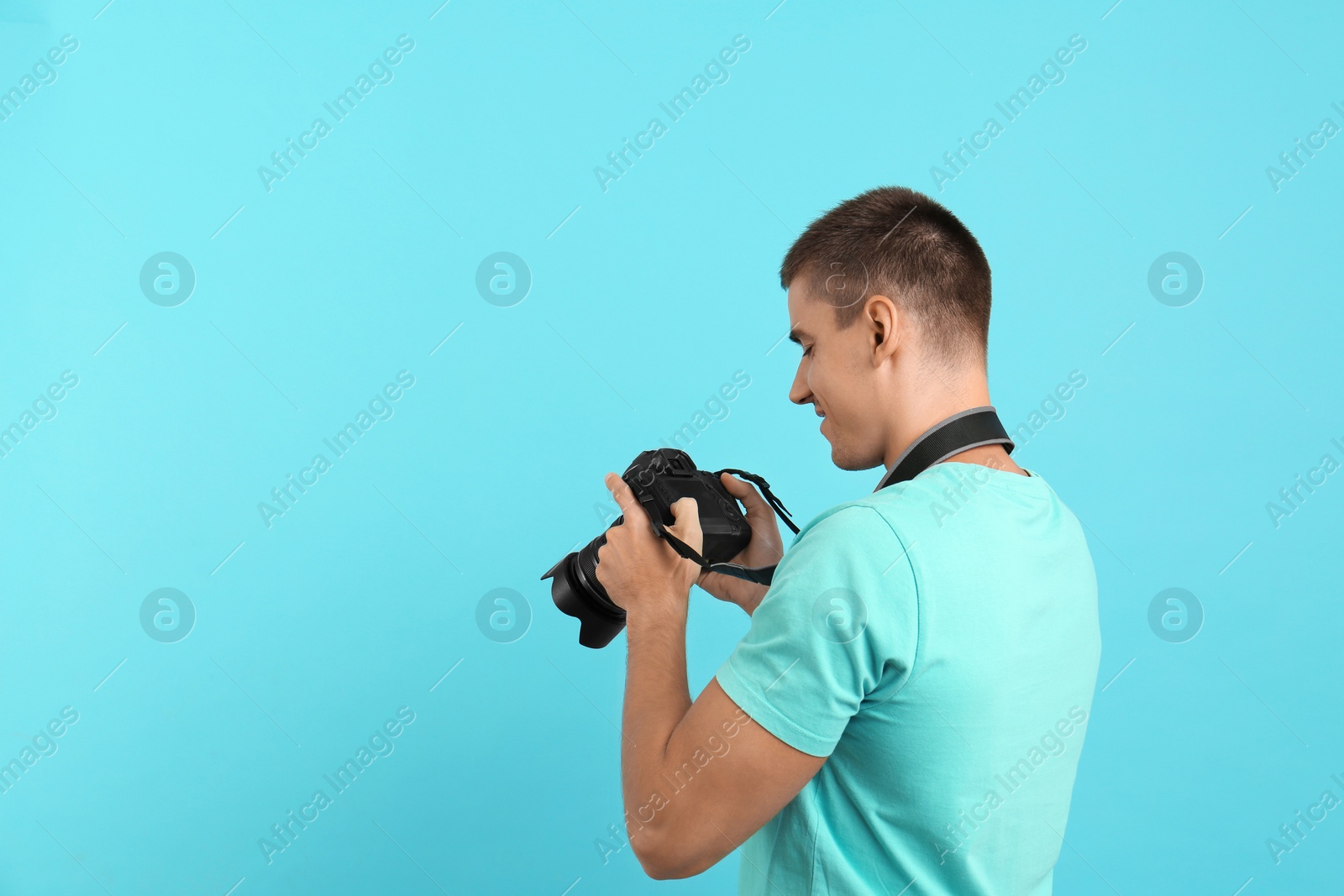 Photo of Young photographer with professional camera on light blue background. Space for text