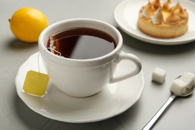 Photo of Tea bag in ceramic cup of hot water and sugar on grey table