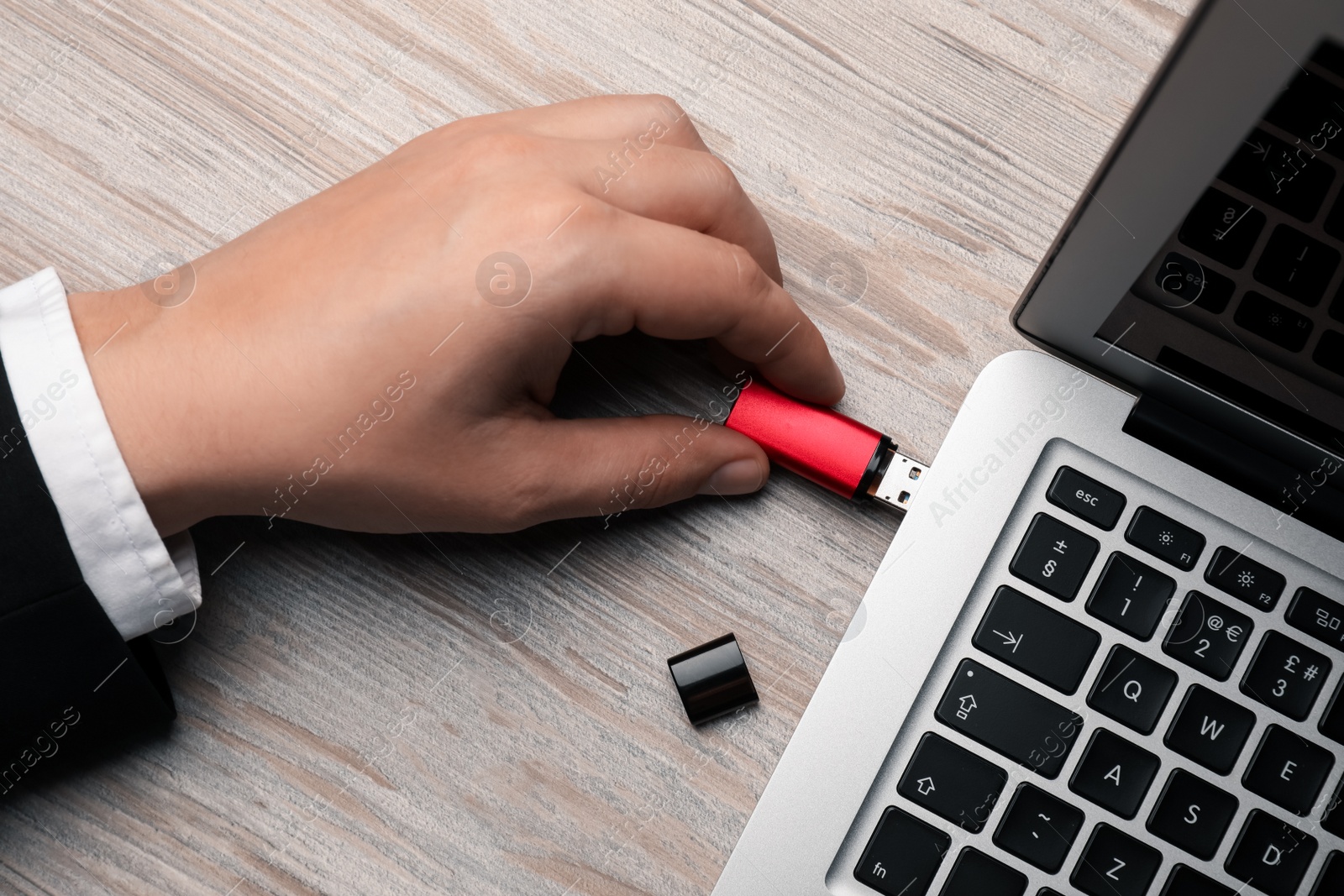 Photo of Man connecting usb flash drive to laptop at white wooden table, top view