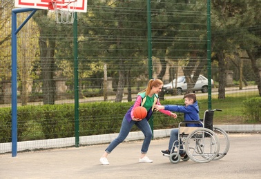 Photo of Preteen boy in wheelchair and young woman playing basketball on sports ground