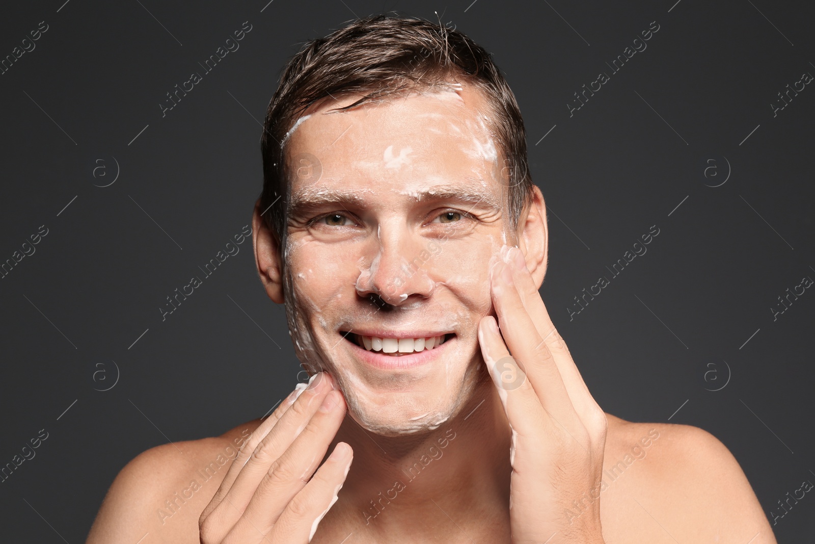 Photo of Man washing face with soap on dark background