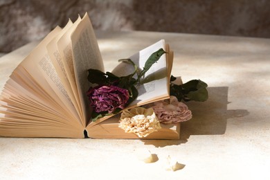 Book with beautiful dried flowers on light table, space for text