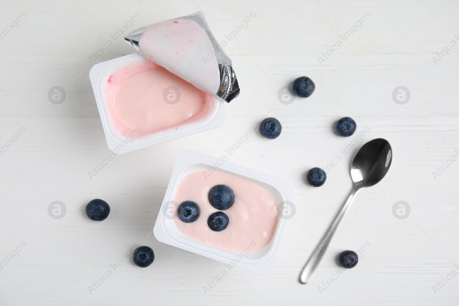 Photo of Plastic cups with tasty yogurts and blueberries on white wooden table, flat lay