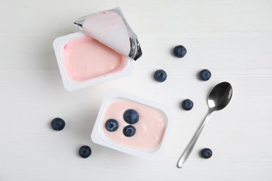 Plastic cups with tasty yogurts and blueberries on white wooden table, flat lay