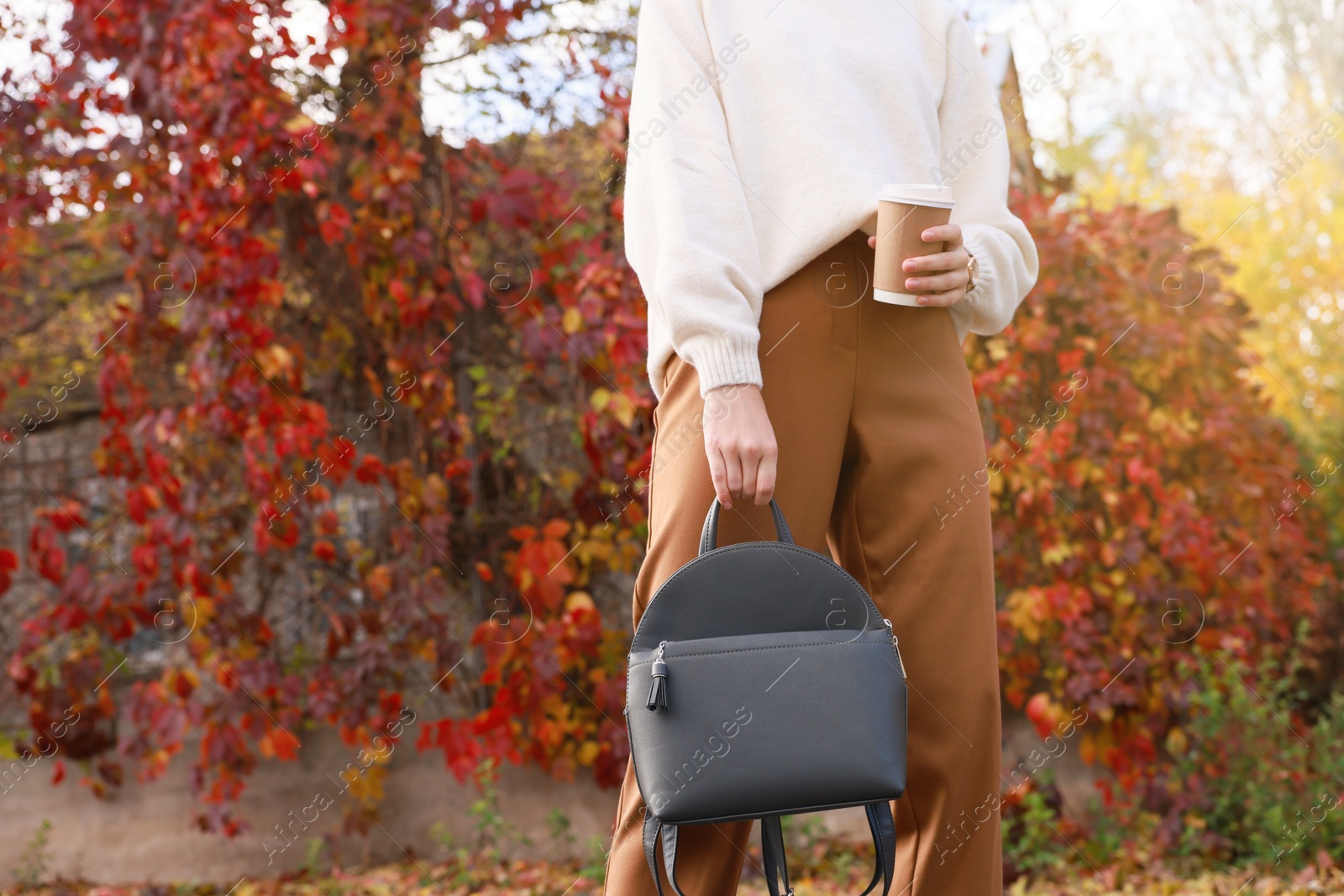 Photo of Young woman with stylish grey backpack and hot drink in autumn park, closeup
