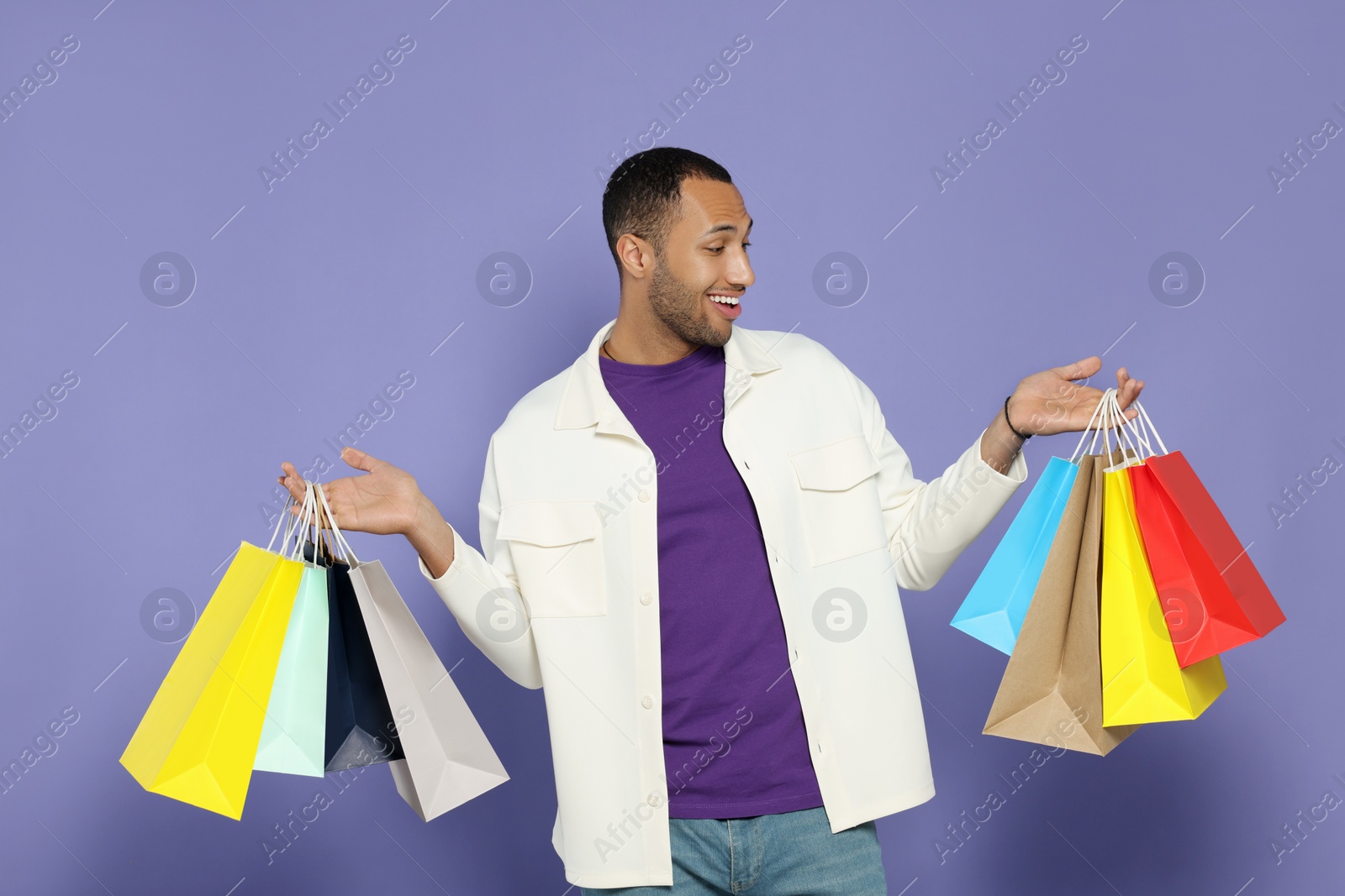 Photo of Happy African American man with shopping bags on purple background