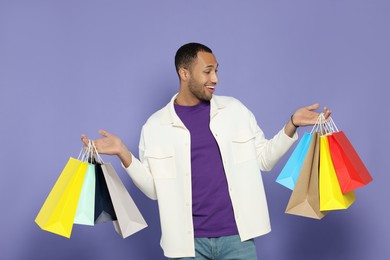 Happy African American man with shopping bags on purple background