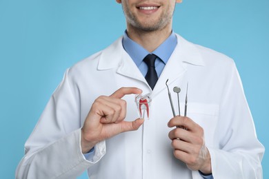 Dentist holding tooth model and tools on light blue background, closeup