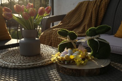 Photo of Terrace with Easter decorations. Bouquet of tulips in vase, bunny figures, decorative nest and eggs on table outdoors